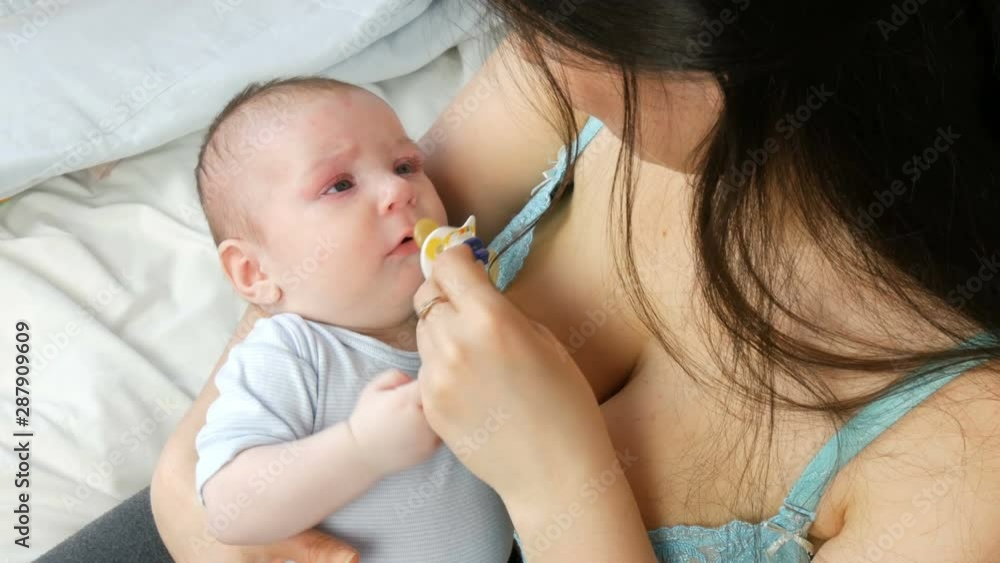 A two-month newborn baby lies on the mother arms and sucks the nipple. Mother tries to put her child to sleep A two-month newborn baby lies on the mother arms and sucks the nipple. Mother tries to put her child to sleep