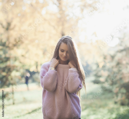 Happy young woman in park on sunny autumn day. Cheerful beautiful girl in sweater outdoors 