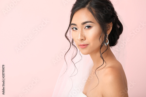Beautiful young Asian bride on color background