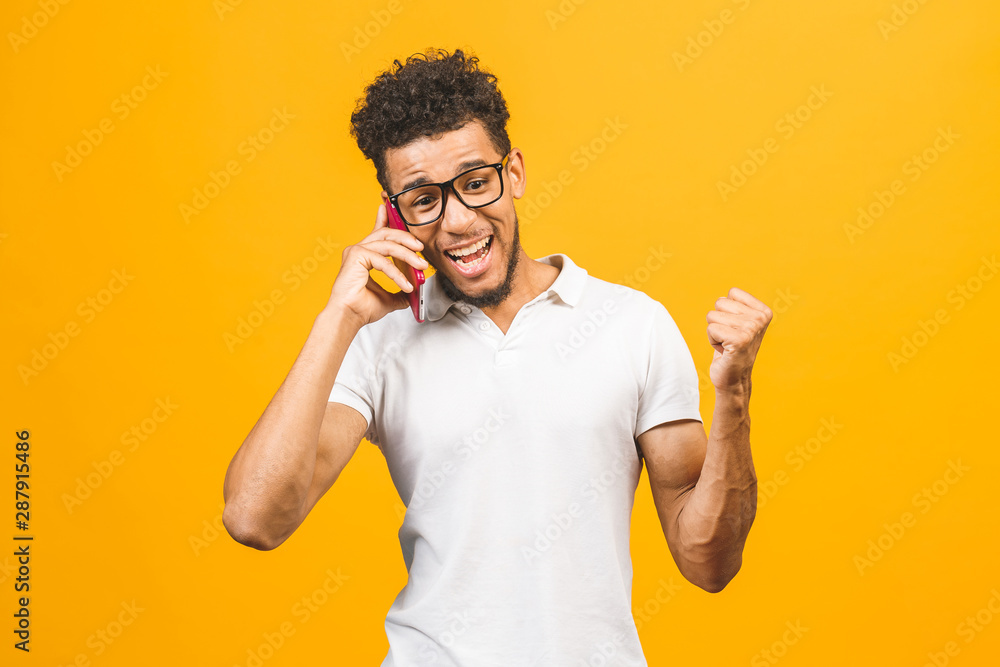 Happy winner. Portrait of a cheerful african american guy talking on mobile phone isolated against yellow background. Happy winner. Portrait of a cheerful african american guy talking on mobile phone isolated against yellow background.