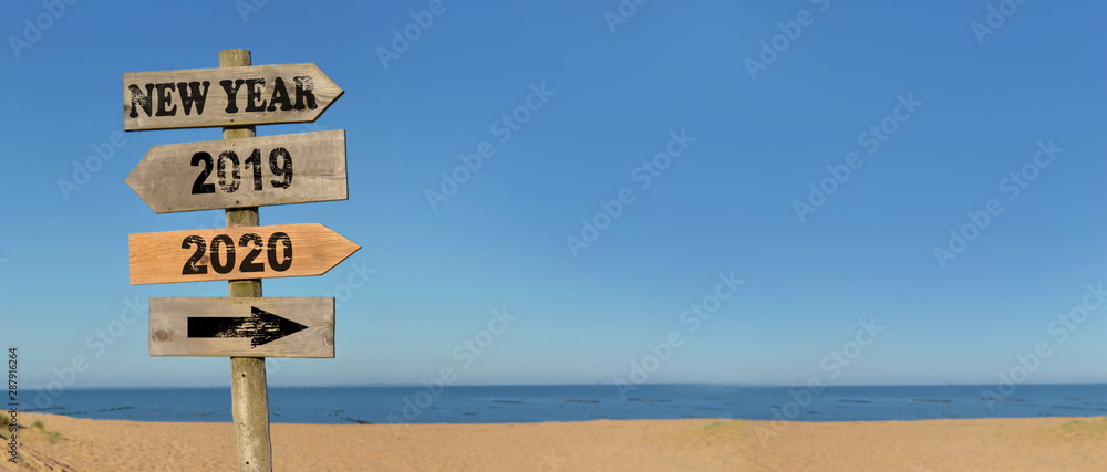 wooden signpost happy new year on the beach with opposed arrows  2020 and 2019