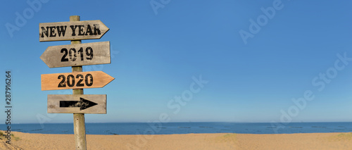 wooden signpost happy new year on the beach with opposed arrows  2020 and 2019