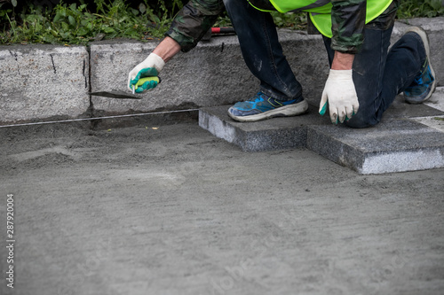Close up of the gloved hands of a builder laying outdoor paving slabs on a prepared base.
