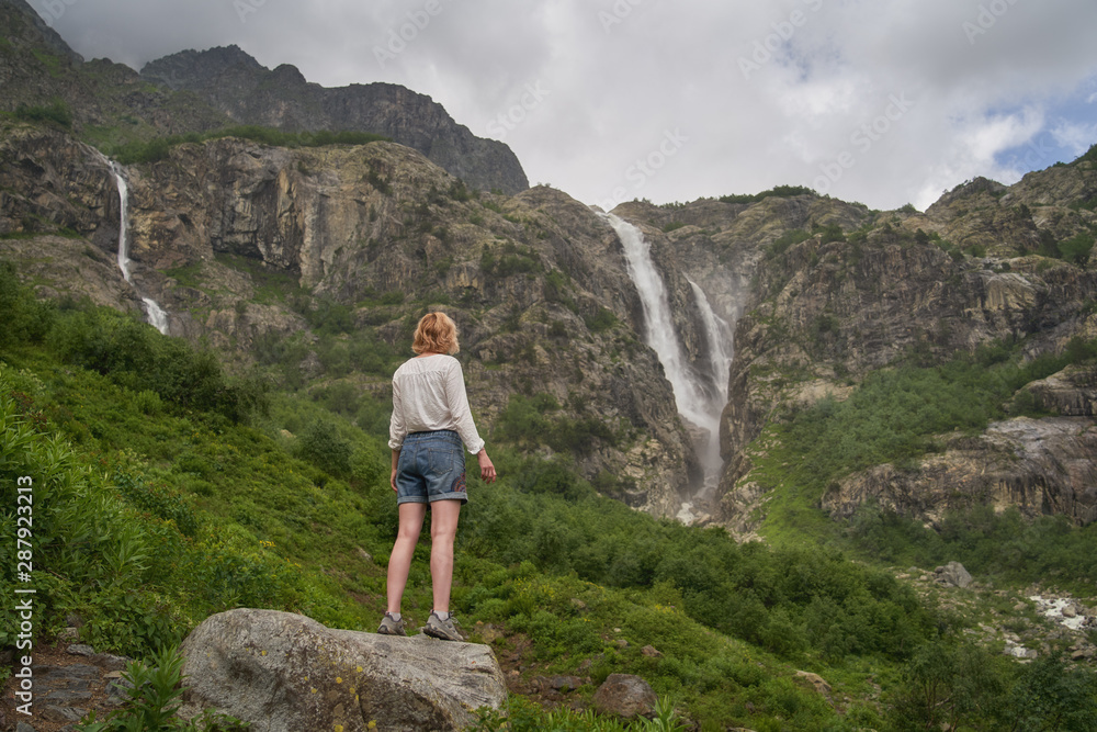 Woman standing on the rock and enjoying the view of epic waterfall 