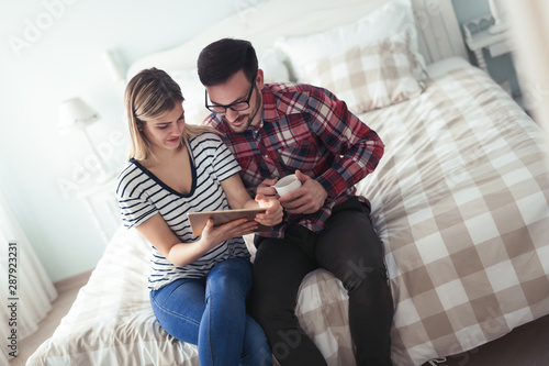 Happy couple using digital tablet in bedroom