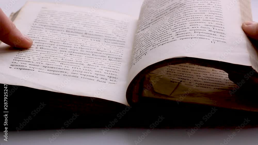 The man opens and flips through an old book, turning the pages close-up in slow motion