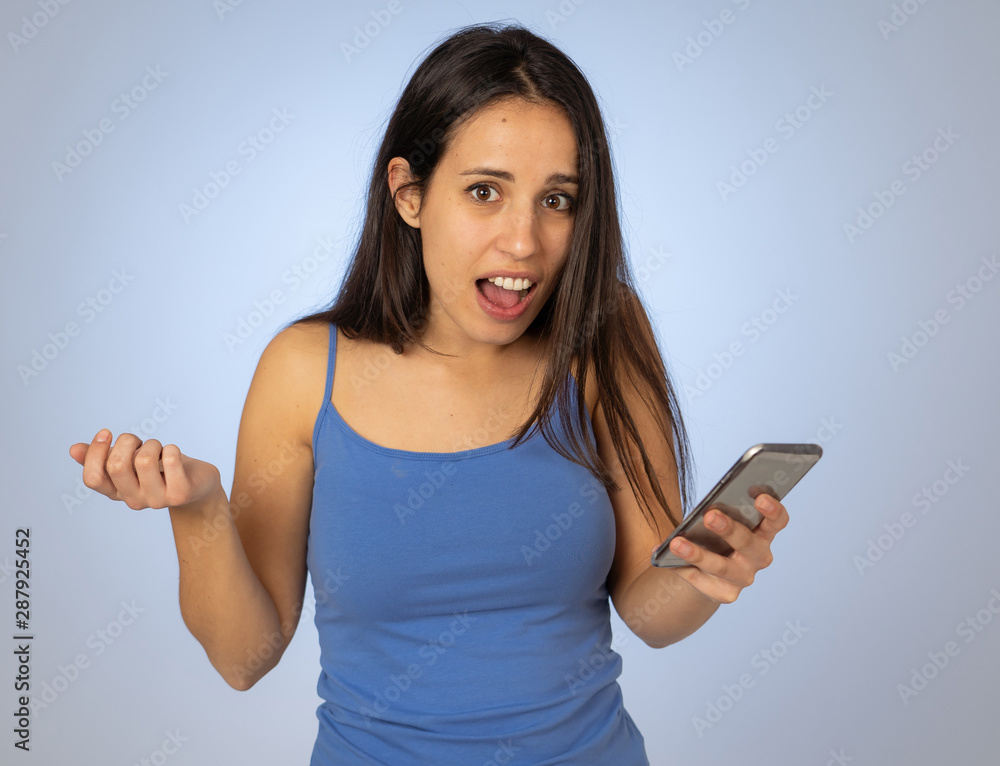 Attractive young woman looking at mobile smart phone shocked and surprised having lost of likes Attractive young woman looking at mobile smart phone shocked and surprised having lost of likes