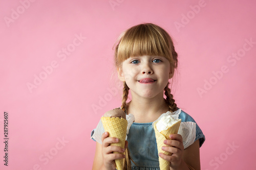 little girl with pigtails in a blue dress eating ice cream in a cone on a pink background