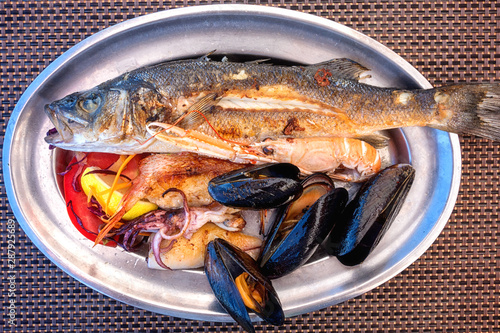 Traditional Mediterranean grilled seafood dish, plate with fish, shrimp, squid, mussels, lemon and salad, served food, top view photo