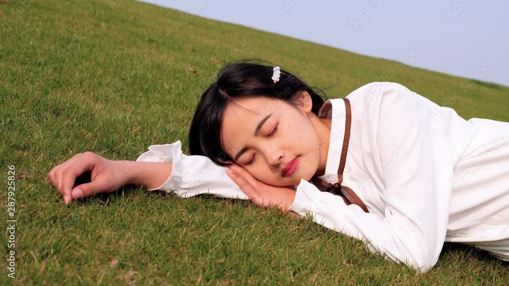 Close up portrait of a beautiful Chinese young woman in white shirt lying on green grass field with eyes closed, enjoy the spring breeze and have a good dream, 4k footage, slow motion. Close up portrait of a beautiful Chinese young woman in white shirt lying on green grass field with eyes closed, enjoy the spring breeze and have a good dream, 4k footage, slow motion.