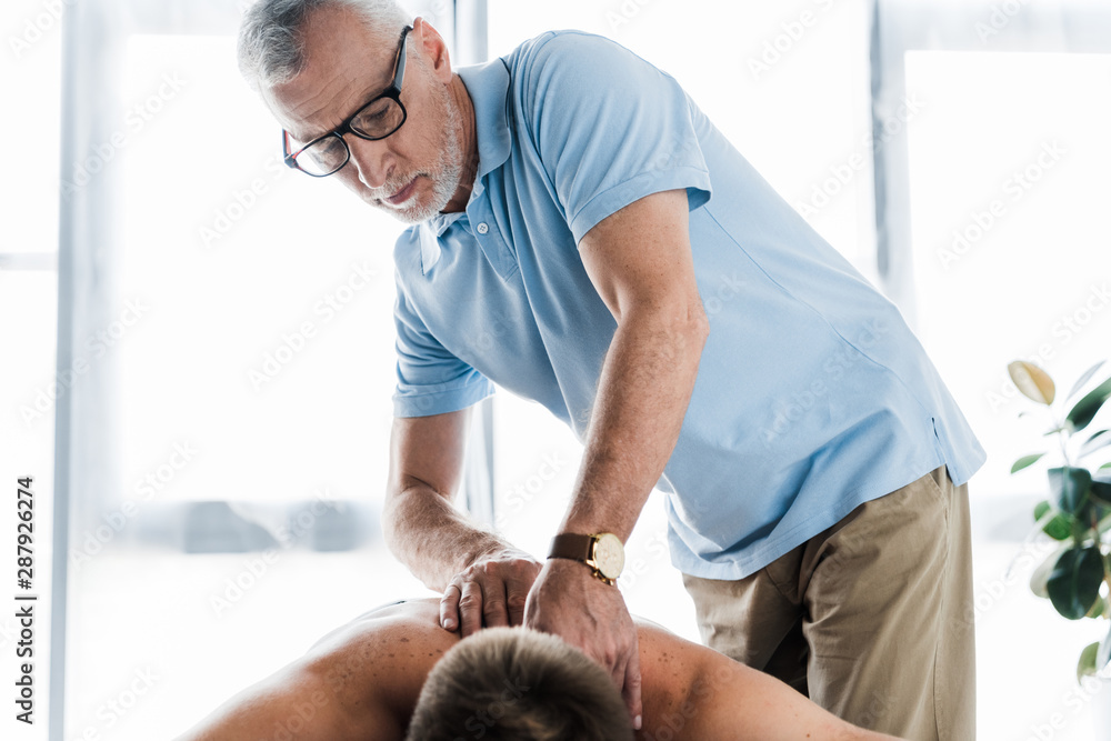 Obraz premium bearded chiropractor in glasses doing massage to shirtless patient on massage table