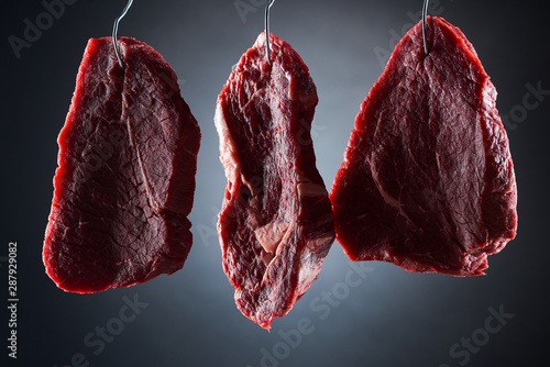 Foto raw beef steaks on metal hooks on dark black background