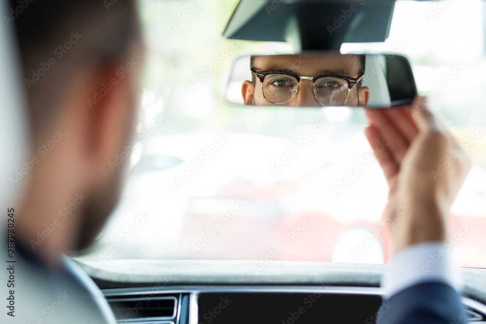Obraz na plátně Businessman fixing rear view mirror before driving his car