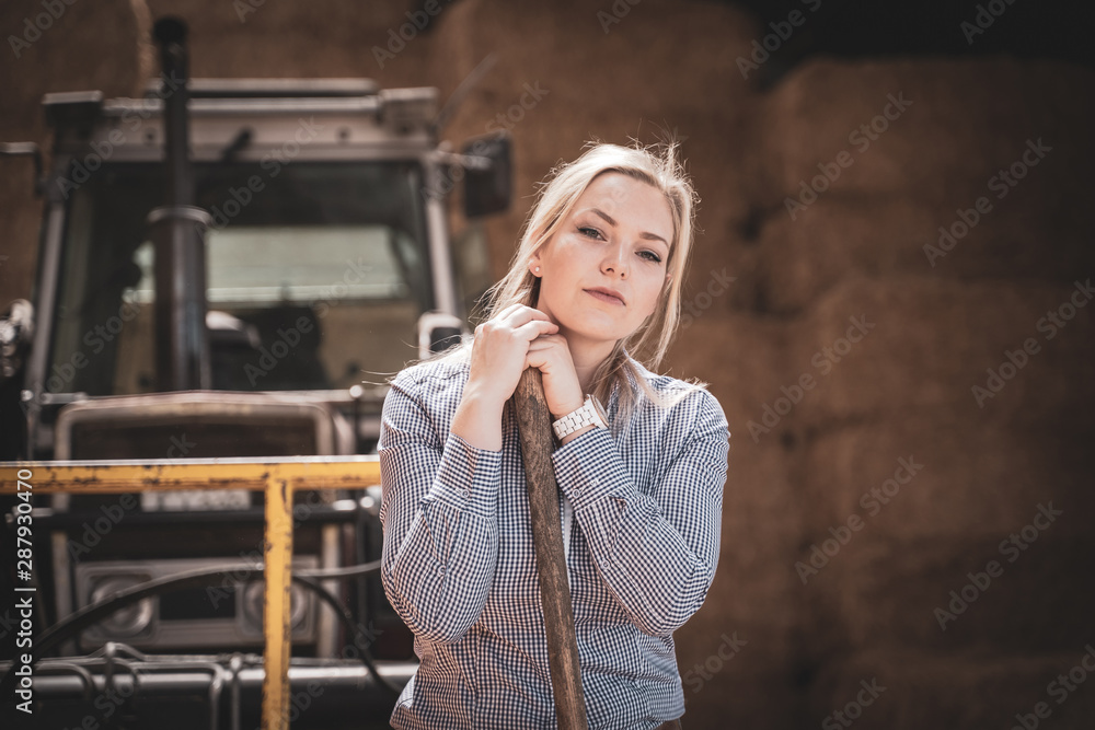 Nachdenkliche, junge Landwirtin vor einem Traktor in einer Strohlagerhalle Nachdenkliche, junge Landwirtin vor einem Traktor in einer Strohlagerhalle