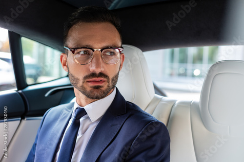 Dark-eyed bearded businessman sitting on back seat in car © zinkevych