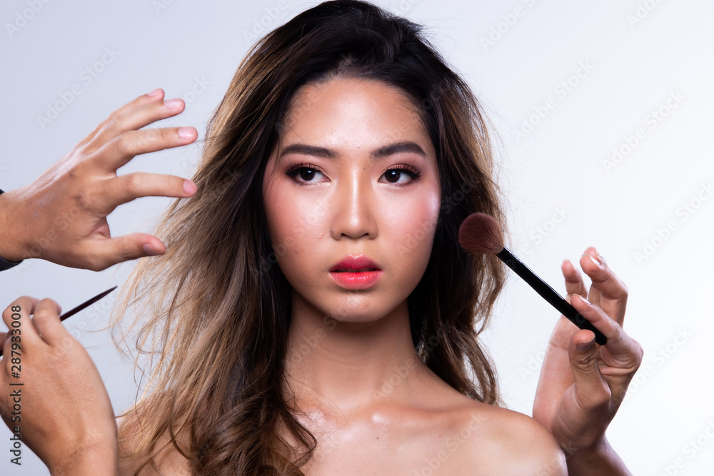 Obraz premium Many Hands helping Magic on Asian Woman black curl hair to be more beautiful with many people, eye shadow lipstick for many spot on big smile face, studio lighting white background isolated
