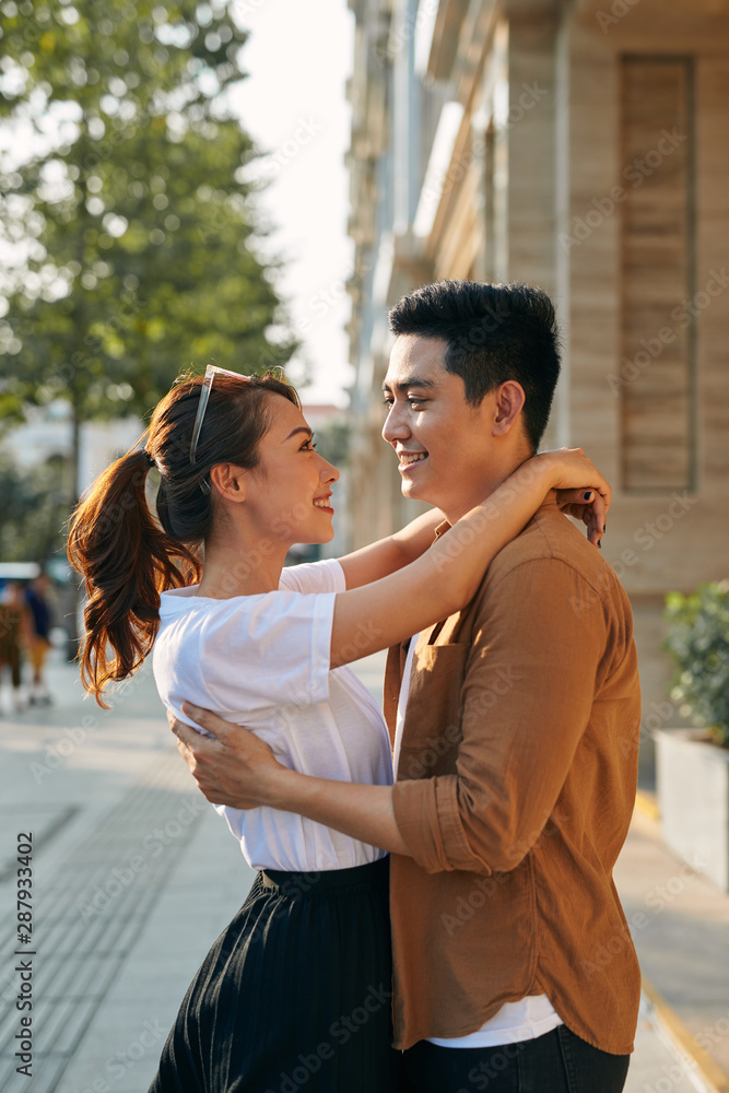 Rear view of a young couple hugging in a destination city while standing in the shopping district near a luxury quality shoe store, outdoors Rear view of a young couple hugging in a destination city while standing in the shopping district near a luxury quality shoe store, outdoors