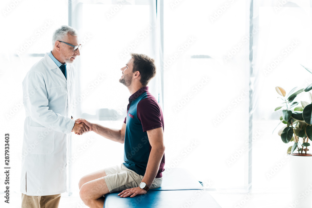 doctor in glasses shaking hands with happy man in clinic doctor in glasses shaking hands with happy man in clinic