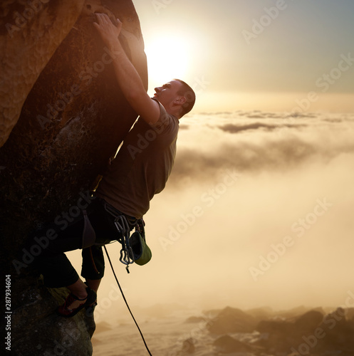 Εκτύπωση καμβά Strong brave climber blinded by sunlight on high natural rock wall