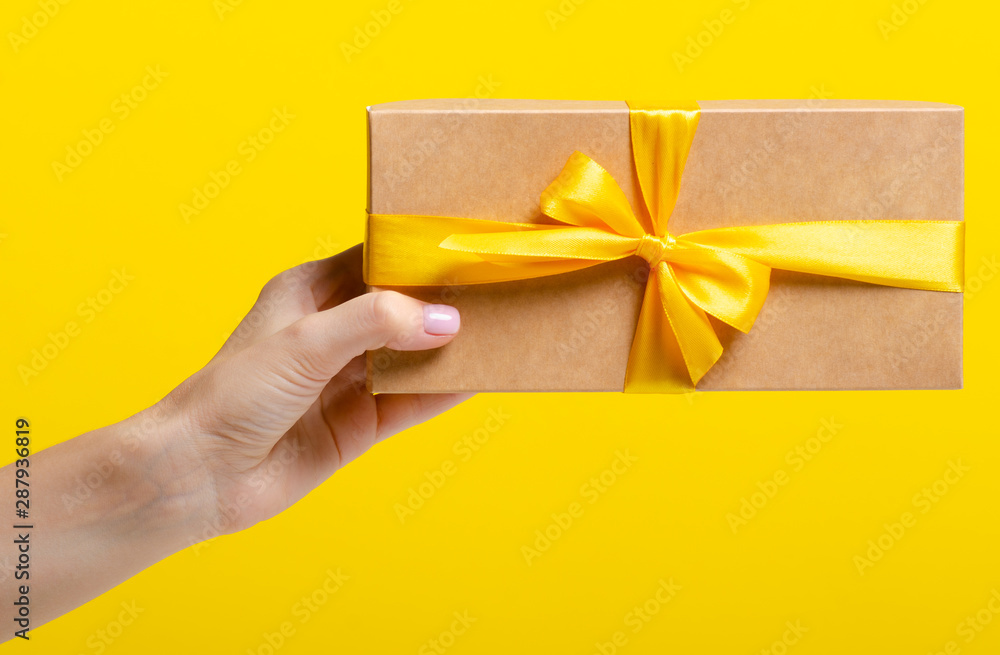 Gift box with yellow ribbon in hand on yellow background Gift box with yellow ribbon in hand on yellow background