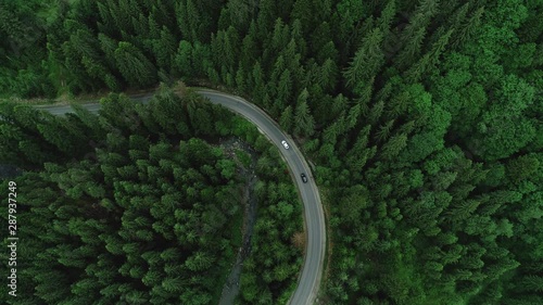 Two cars are passing at a mountain road in the woods near the river flows