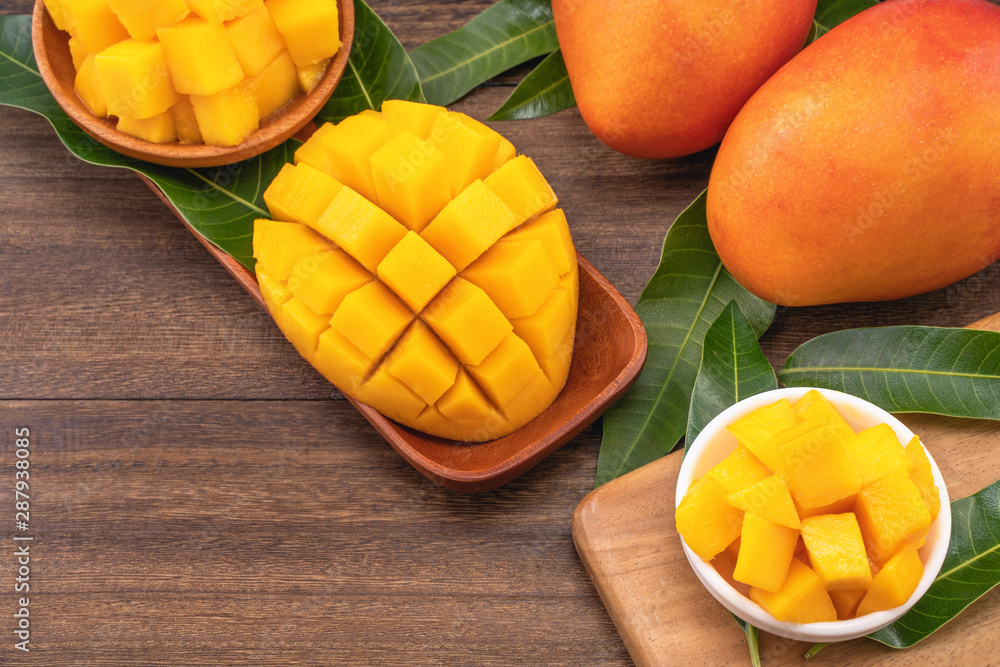 Fresh mango, beautiful chopped fruit with green leaves on dark wooden table background. Tropical fruit design concept. Flat lay. Top view. Copy space Fresh mango, beautiful chopped fruit with green leaves on dark wooden table background. Tropical fruit design concept. Flat lay. Top view. Copy space