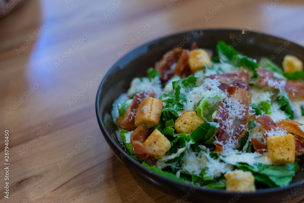 Caesar Salad with bacon in black plate on wooden background