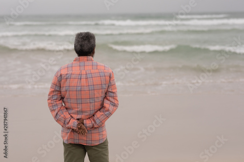 Senior man with hands behind back standing on the beach
