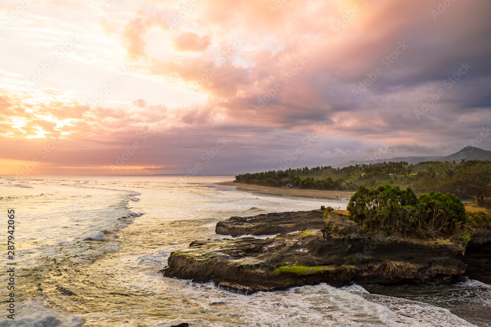 Dramatic aerial sunset over a black sand coastline with rocks in Bali, Indonesia