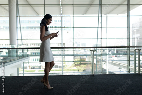 Free Download Side view of businesswoman using mobile phone in office and walking on a carpet walkway - GFXLoad