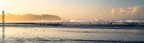 Sunrise panoramic over a tropical coastline with light catching the surf spray, Bali, Indonesia