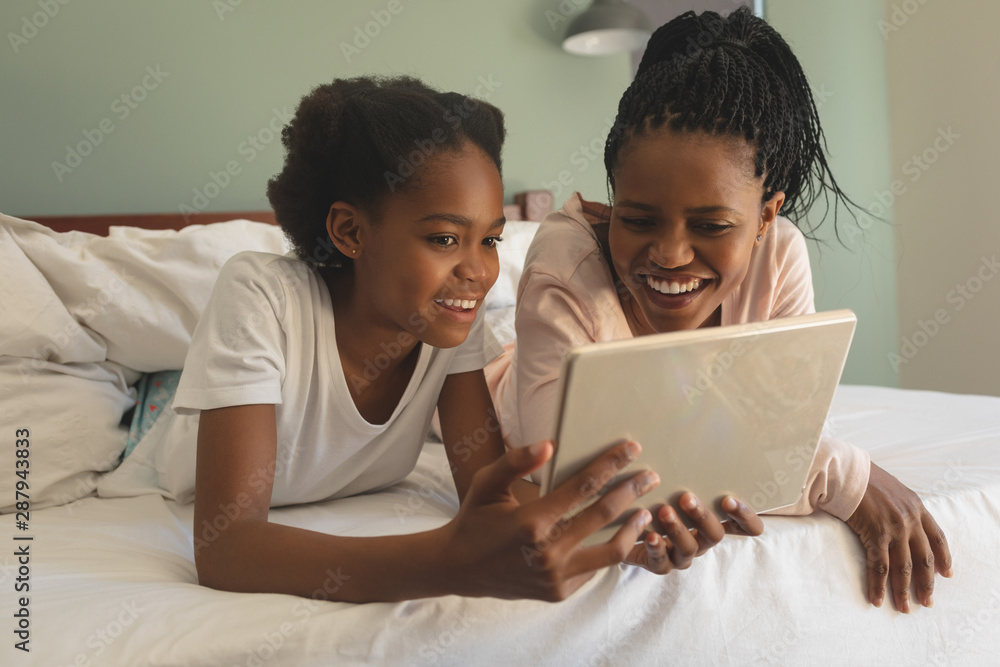 Happy African American mother and daughter lying on bed and using digital tablet Happy African American mother and daughter lying on bed and using digital tablet