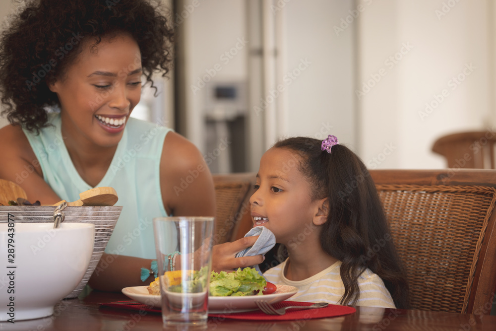 African American mother wiping her daughter mouth with napkin at dining table African American mother wiping her daughter mouth with napkin at dining table
