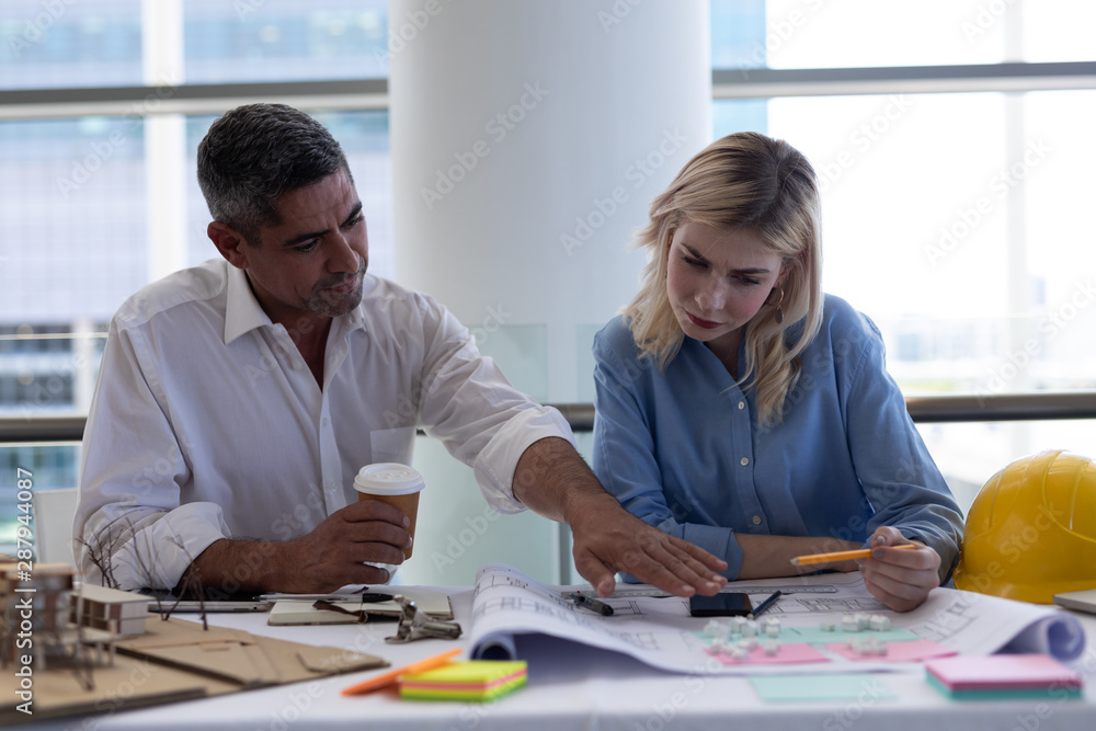 Fototapeta premium Caucasian architects discussing over blueprint at desk in office