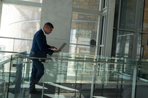 Side view of a handsome businessman working on his laptop on the first floor walkway of the office 