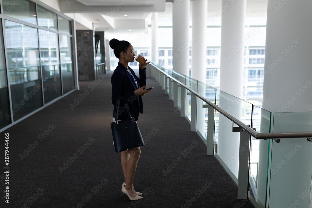 Young mixed-race businesswoman having coffee while using mobile phone in office