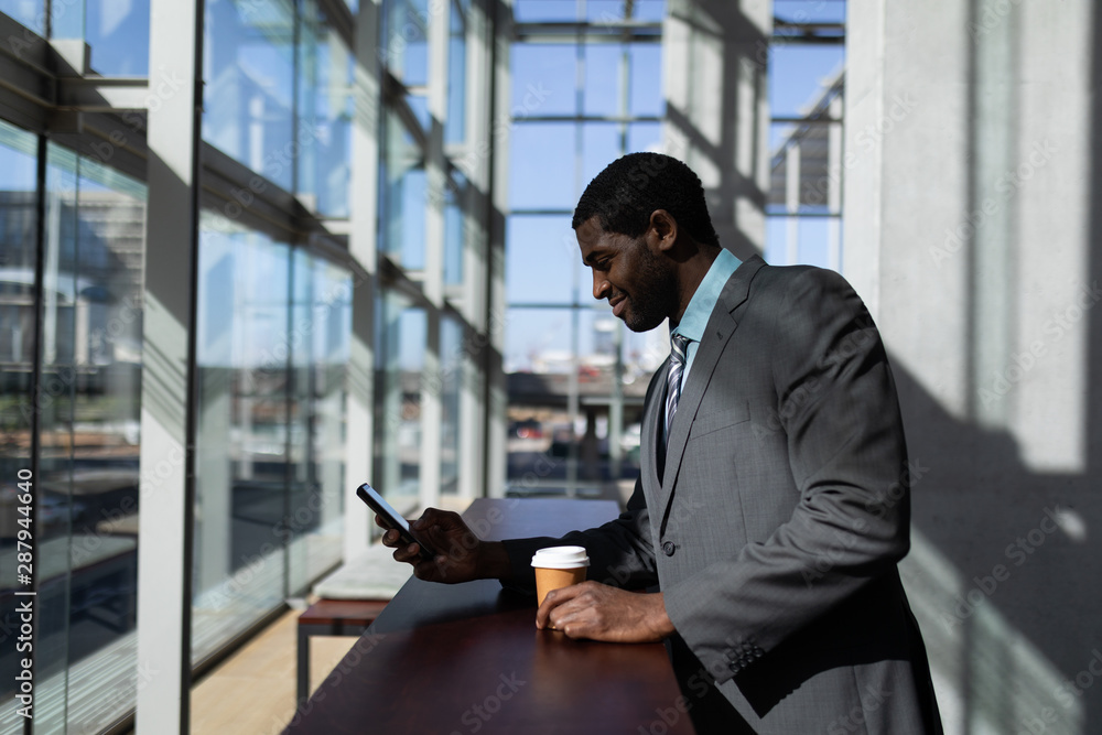African-American businessman with coffee cup using mobile phone in office African-American businessman with coffee cup using mobile phone in office