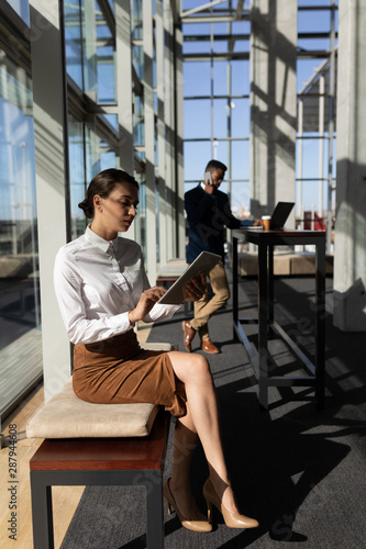 Caucasian businesswoman using digital tablet while sitting on bench in office