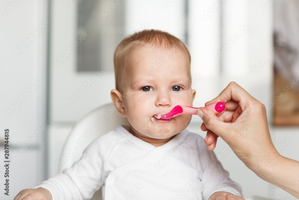 Feeding of cute baby with a spoon in the kitchen Feeding of cute baby with a spoon in the kitchen