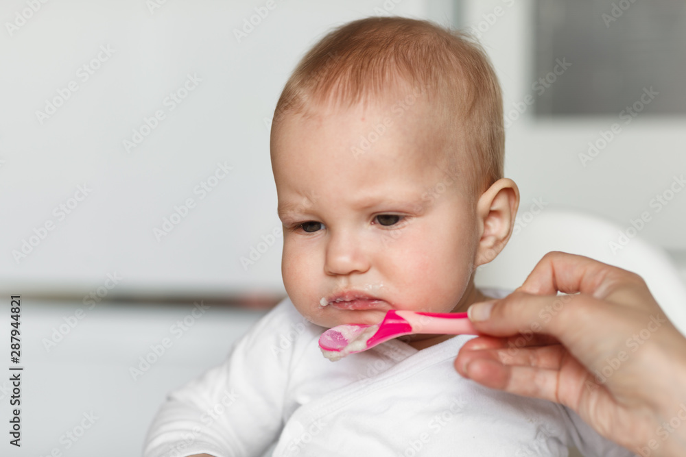 Feeding of baby with a spoon in the kitchen. Refusal of food Feeding of baby with a spoon in the kitchen. Refusal of food