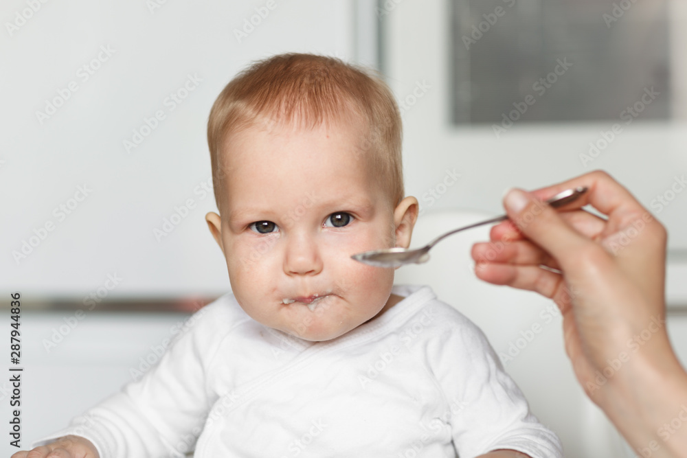 Feeding of cute baby with a spoon in the kitchen Feeding of cute baby with a spoon in the kitchen