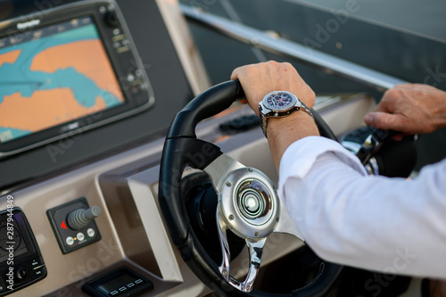 A man runs a yacht. A person sits behind the wheel of the boat