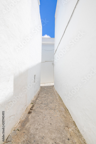 vertical shot of pedestrian alley narrowing in famous Andalusian old town, with typical arabic white houses, named Vejer de la Frontera (Cadiz, Andalusia, Spain, Europe)