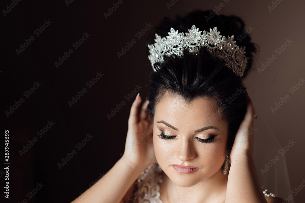  Portrait of beautiful bride with stylish make up and hair style. A elegant and beautiful bride at home. A bride in a dress corrects the crown. Pretty young girl. Wedding.  Sexy bride.