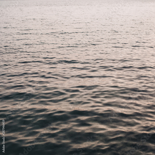 Sea or ocean water with little relaxing waves and reflection in different light. Beautiful gradient with creamy pink and dark blue colors. Neutral background and texture.