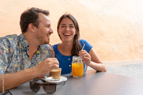 Young couple laugh while drink a smoothy and a coffee. Husband and Wife smiling, sitting in a bar. Lovers together, dating and flirting in a lounge.