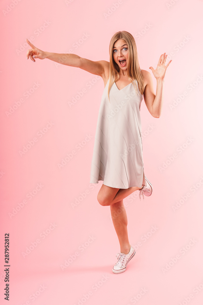 Full length image of happy blond woman expressing wonder and pointing finger at copyspace Full length image of happy blond woman expressing wonder and pointing finger at copyspace