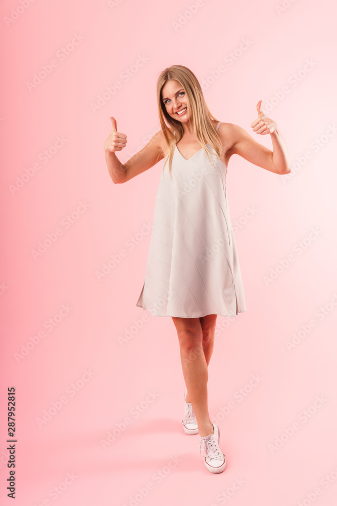 Full length image of gorgeous young woman wearing dress smiling at camera and showing thumbs up