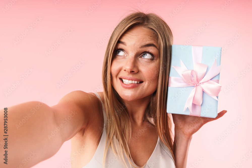 Image of lovely young woman wearing dress smiling and holding gift box while taking selfie photo Image of lovely young woman wearing dress smiling and holding gift box while taking selfie photo