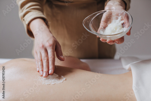 Hands of unrecognisable woman masseuse applying skin scrub on client's back. photo